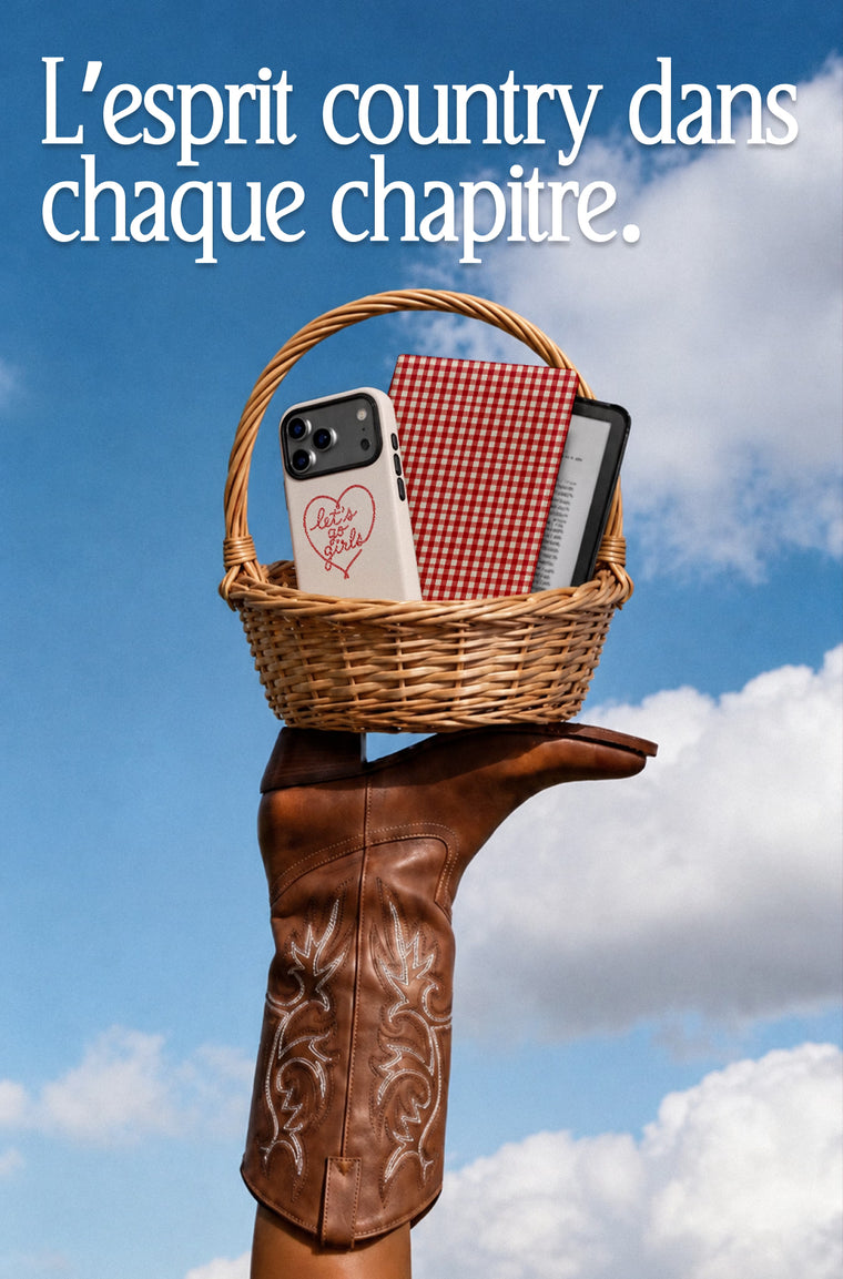 A hand wearing a brown western boot holds a wicker basket containing a phone case with a red heart design, a red-and-white gingham notebook, and a black smartphone against a blue sky with clouds. French text appears at the top: 'L'esprit country dans chaque chapitre.