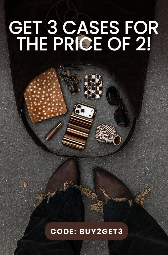 A promotional flat-lay showing a black bag opened on gray pavement, with several fashion accessories arranged inside: a brown polka-dot clutch, a striped phone case, a small patterned case, sunglasses, a lip balm, and a striped wristlet. Large text at the top reads 'GET 3 CASES FOR THE PRICE OF 2!' and a brown label at the bottom says 'CODE: BUY2GET3'.